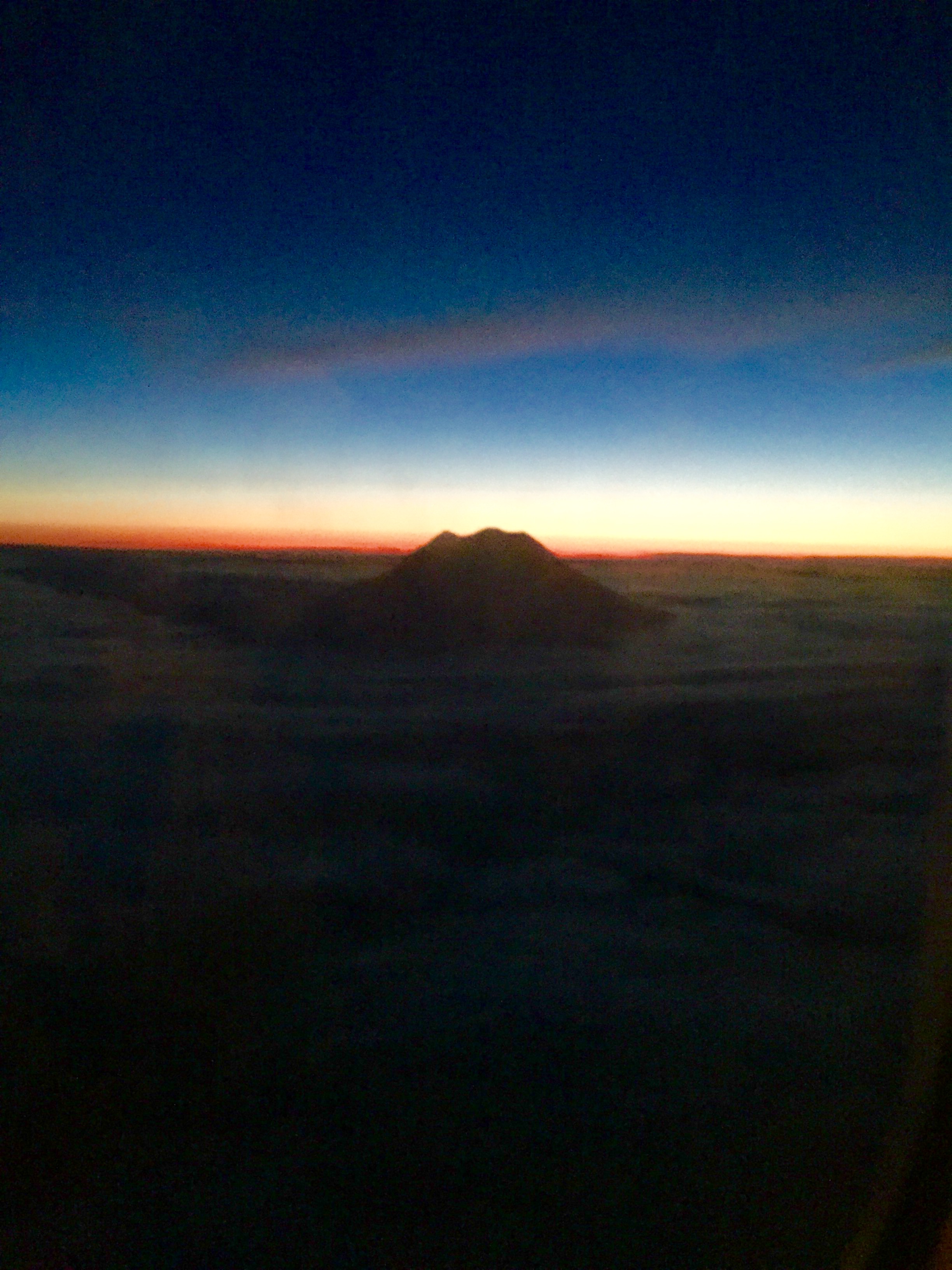 Dark mountain silhouette at dawn beneath a blue horizon.